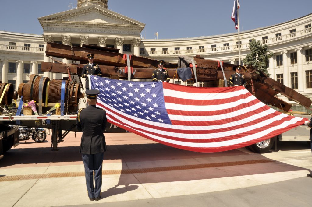 US flag held in front of steel wreckage from the 9/11 tragedy